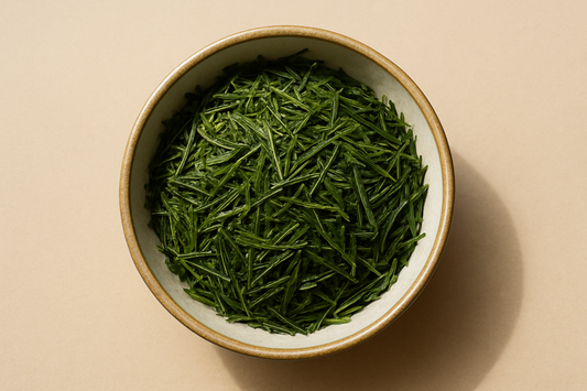 Photorealistic top-down photograph of a round beige ceramic bowl with an off-white interior, filled with loose Sencha green tea leaves (long, thin, needle-like bright green leaves). The bowl is centered on a soft matte beige background, with soft natural daylight and gentle shadows, ultra-detailed and realistic.
